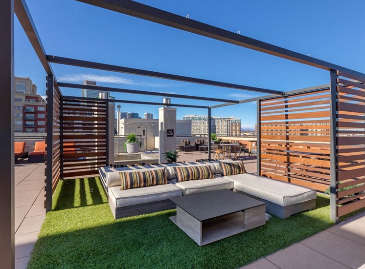 Rooftop Terrace Lounge with Cushioned Patio Sectional  on Grass with Patio Coffee Table Surrounded by Decorative Metal and Wood Partial Enclosure, with Orange Cushioned Lounge Chairs and City View in the Background